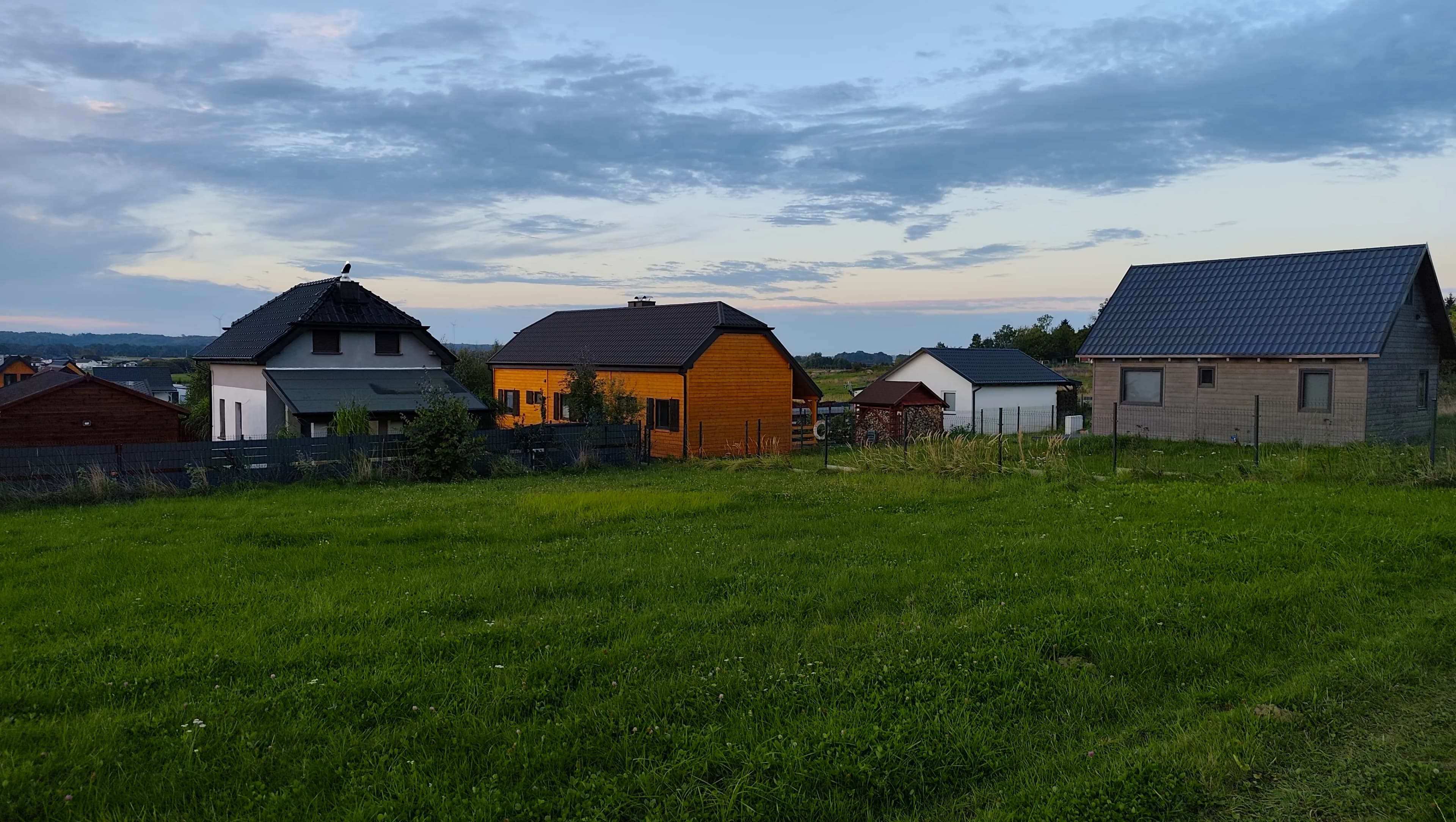 Pomarańczowy drewniany domek Mat widziany z łąki wieczorem